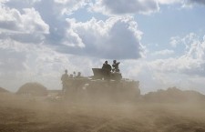 Ukrainian army servicemen around an armoured vehicle are seen through dust raised by passing vehicles near Debaltseve